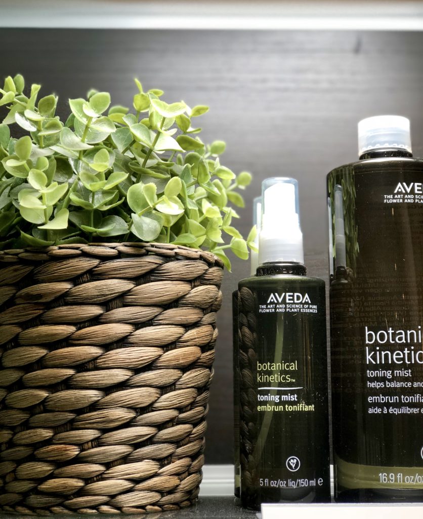 This is a picture of two Aveda products on a shelf in the salon. Next to the products is a basket with a light green plant in it. 